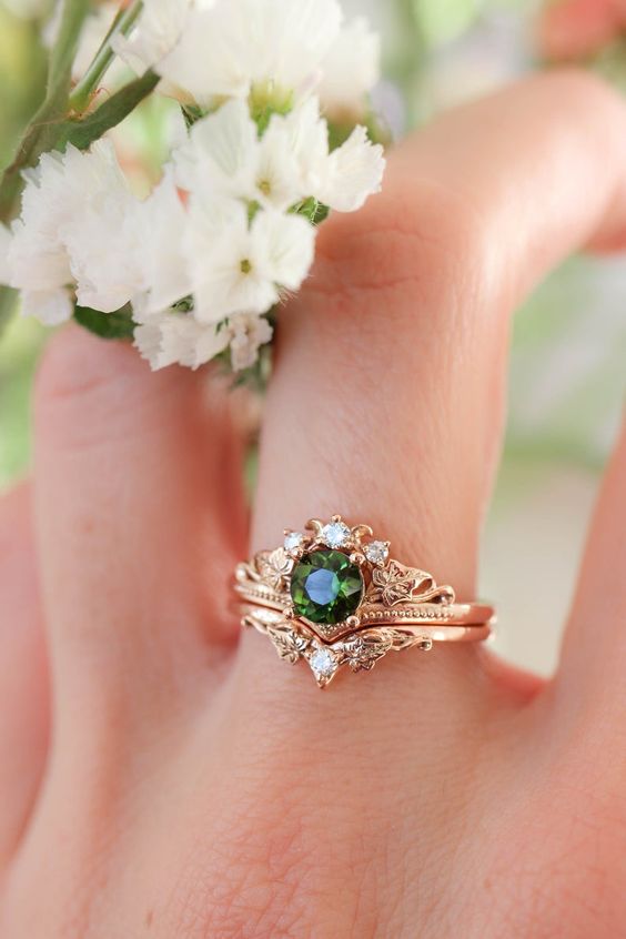 a lovely stacked engagement ring with a central round emerald, an upper ring with diamonds and a lower ring with a single one