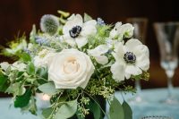 a lovely wedding centerpiece of white roses and anemones, greenery, blue blooms and allium plus eucalyptus and candle is a chic idea