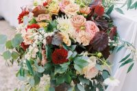a lush and bold fall wedding centerpiece of greenery, blush, deep red and peachy blooms and dark foliage is chic