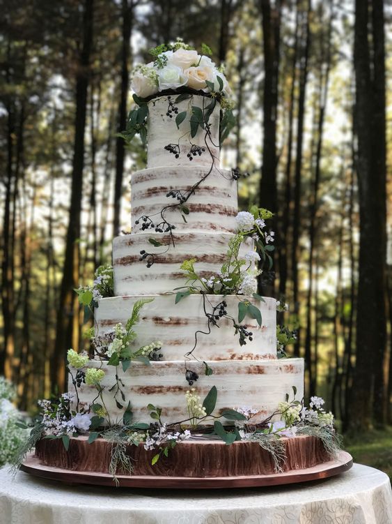 a naked wedding cake decorate with greenery and white roses on top is a perfect solution for an enchanted forest wedding