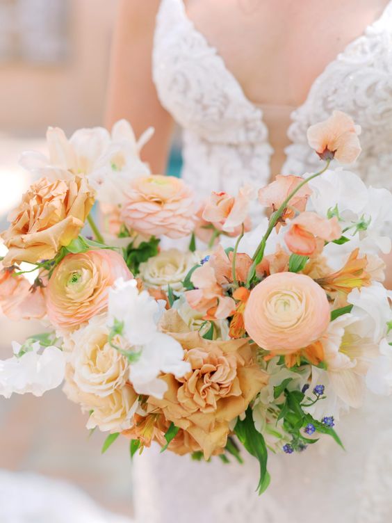 a peach wedding bouquet with peachy raunuculus, roses, white fillers and some blue blooms is a cool solution