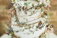 a pretty enchanted forest wedding cake with light green buttercream tiers, with twigs, blooms, berries and greenery plus some feathers is a great idea