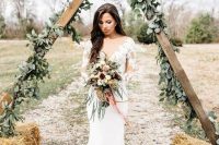 a pretty rustic triangle wedding arch covered with greenery and with hay at the base is a cool solution for a rustic boho wedding