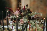 a refined moody secret garden wedding centerpiece of blush and dark blooms, greenery, berries and feathers is amazing for the fall