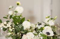 a refined wedding centerpiece of white blooms of various kinds including anemones, greenery and berries and candles around is very cool