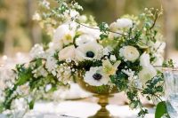 a refined wedding centerpiece of white ranunculus, anemones, blooming branches and greenery in a chic gilded bowl is perfect for spring or summer