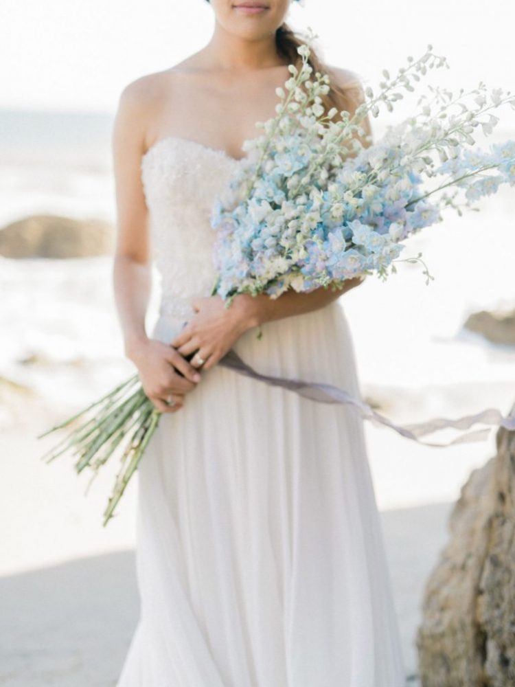 a romantic coastal bridal look with a strapless embellished wedding dress and a white and blue long stemmed wedding bouquet