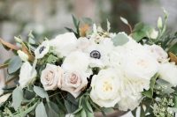 a romantic wedding centerpiece of a dark bowl, white and blush roses, white anemones and greenery plus candles around