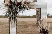 a rustic wedding arch covered with siding, pampas grass, white, blush and dark purple blooms and greenery for a farmhouse wedding