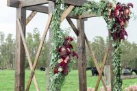 a rustic wedding arch decorated with greenery, blush and burgundy blooms is a lovely idea for a fall rustic wedding