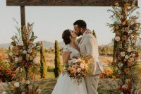 a rustic wedding arch of stained wood, bright and blush blooms, greenery, pampas grass and twigs is very textural and dimensional