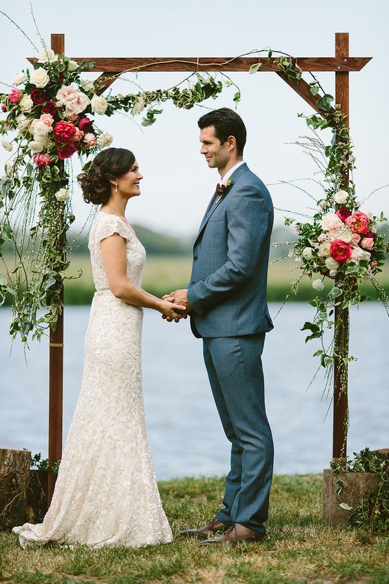 a rustic wedding arch of wood, with greenery, white, pink and burgundy blooms and with a lovely lake view