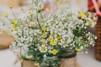 a rustic wedding centerpiece of a wood slice, jars wrapped with twine, daisies and baby’s breath is a very cozy idea