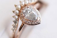 a sophisticated rose gold stacked engagement ring with a pear-shaped diamond framed with mini diamonds and with an arched diamond and pearl ring