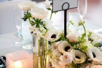 a stylish and elegant wedding centerpiece of white ranunculus and anemones, candles, petals on the table and a card