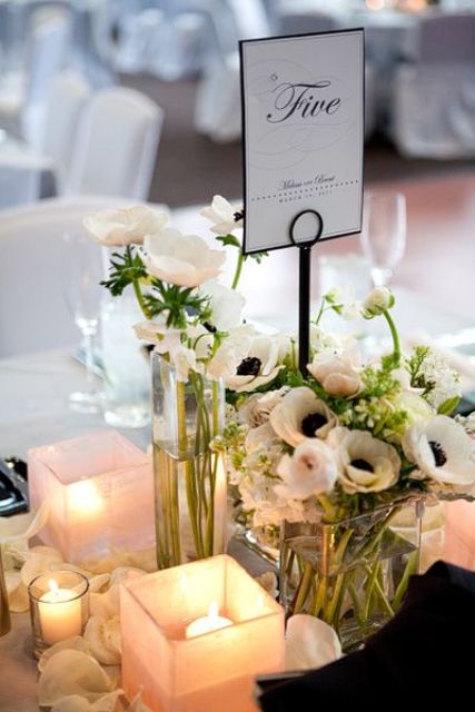 a stylish and elegant wedding centerpiece of white ranunculus and anemones, candles, petals on the table and a card