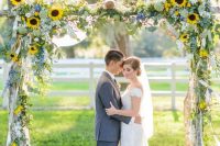 a summer rustic wedding arch of branches, greenery, sunflowers and ribbons plus some blue flowers is a very chic and cool idea