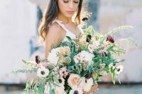 a very textural and dimensional wedding bouquet of lots of greenery, white anemones, peachy, pink and dark blooms and long blue ribbons