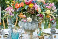 a whimsical secret garden wedding centerpiece in a vitnage bowl, with orange, yellow, pink and lilac blooms and berries plus greenery