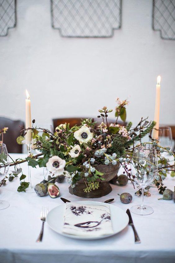 a winter wedding centerpiece of a bowl with white anemones, greenery, branches and twigs and some berries is amazing