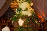 an enchanted forest wedding cake with light green tiers, with greenery, hydrangeas, twigs and moss presented on wooden slices