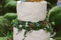 an enchanted forest wedding cake with textural white tiers, moss, greenery, white blooms and leaves plus succulents looks dreamy