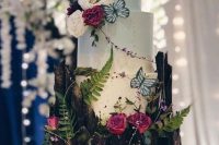an incredible enchanted forest wedding cake looking like a cake growing out of a tree stump, with faux butterflies, natural blooms, mushrooms and greenery plus cool toppers