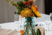 02 a blue mason jar filled with season flowers of football mums, sunflowers, hardy mums, wheat, open roses, and foliage plus gourds