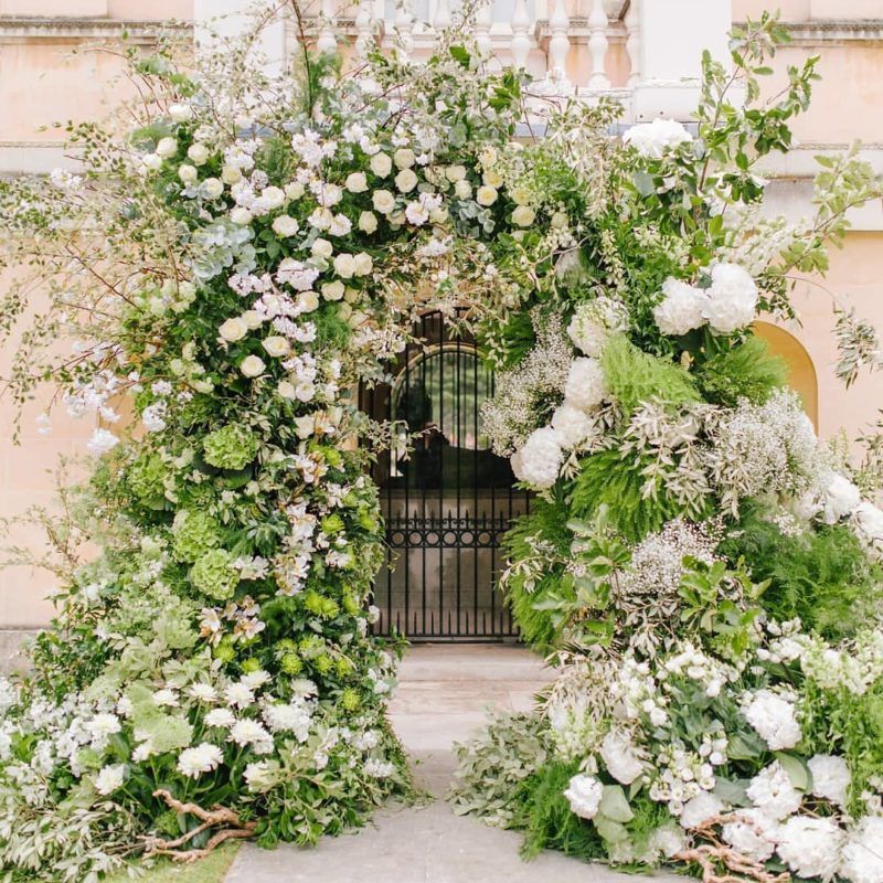A breathtaking overgrown floral wedding arch with lots of textural greenery, twigs and branches and pastel blooms