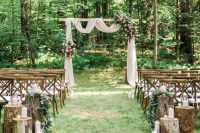 08 a lovely fall backyard wedding ceremony space with an arch with white fabruc, pink and bold blooms and greenery and some tree stump decor