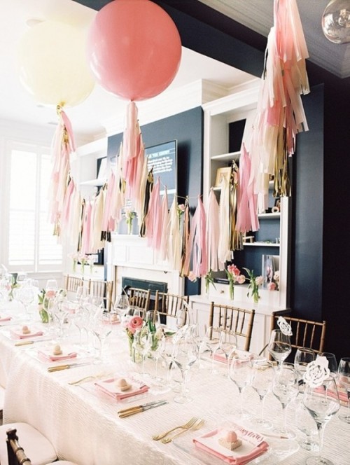 a modern and pastel bridal shower tablescape with pink napkins, pink ranunculus, gold cutlery, elegant glasses and pink tassels over the table