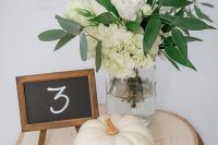 11 a pretty and elegant rustic fall wedding centerpiece of a wood slice, a pumpkin, white roses and hydrangeas and greenery and a chalkboard number