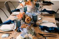 12 a lovely modern chic wedding tablescape with a blue runner, navy napkins and glasses, neutral and rust blooms and greenery, geometric candle lanterns