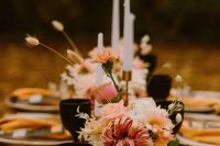 a beautiful fall wedding tablescape with pink blooms and greenery, black and amber glasses, tall candles and mustard napkins