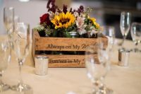 14 a rustic fall wedding centerpiece of a crate, sunflowers, burgundy and deep purple blooms, greenery and candles around
