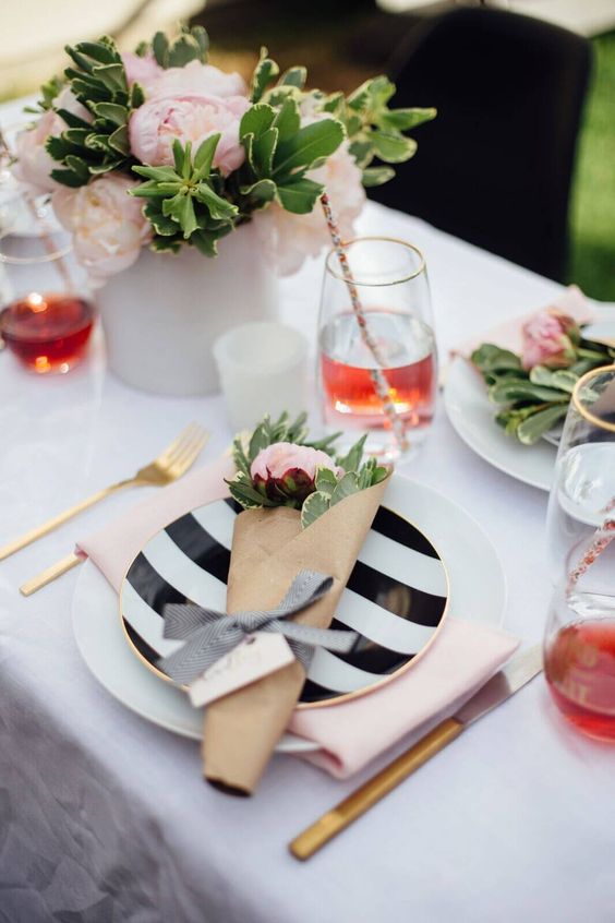 a pretty modern bridal shower tablescape with pink blooms and stripes plus gold cutlery, with candles and blush napkins is chic