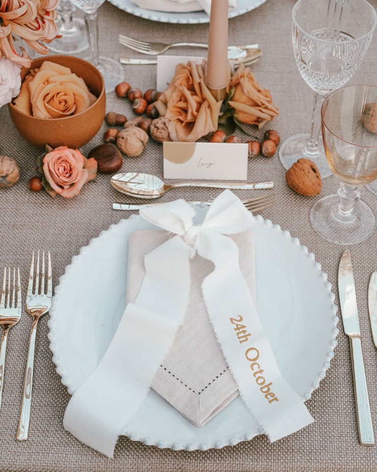 a modern fall wedding tablescape with neutral linens, nuts, pink and peachy roses, pink candles and elegant cutlery