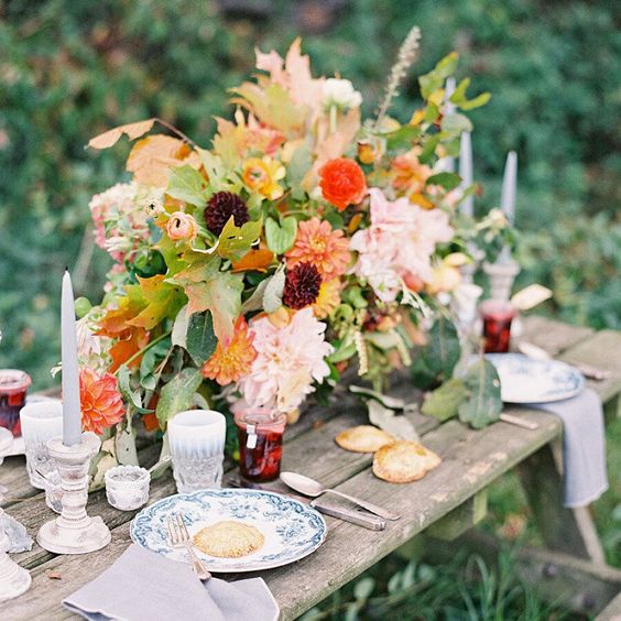 a chic and cool rustic fall wedding tablescape with lush and bright florals, greenery, deep purple and orange blooms, grey candles, printed plates and homemade jam as favors
