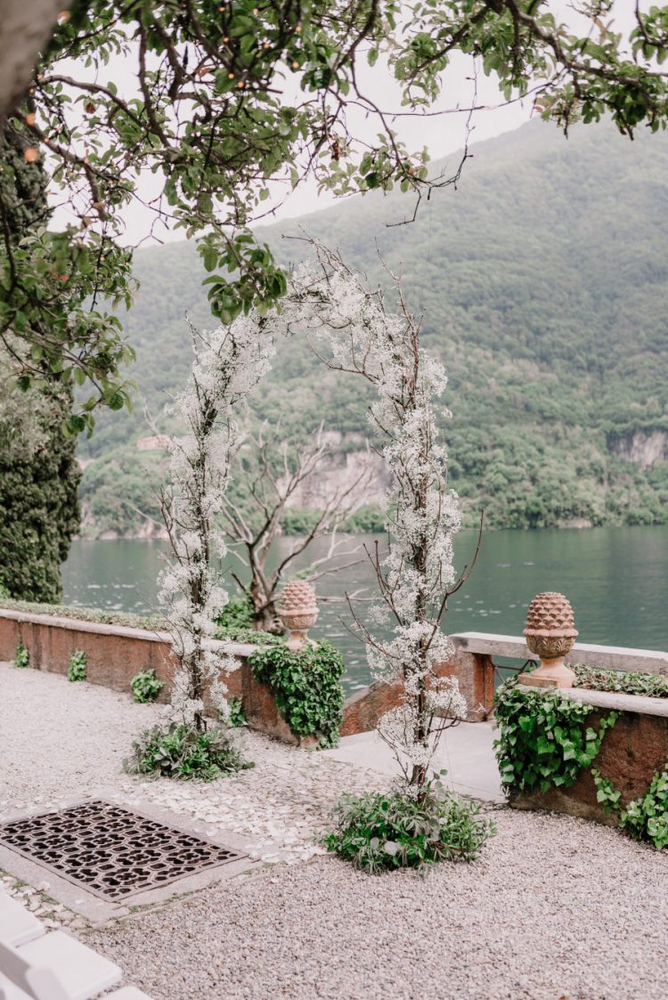 an ethereal wedding arch covered with twigs and lots of white blooms and with a fantastic view of Lake Como is wow