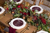 25 a very elegant and refined rustic fall wedding tablescape with a greenery and red rose runner, candles, burgundy menus and napkins plus gold cutlery