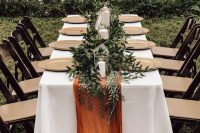 26 a simple modern fall wedding tablescape with gilded chargers, a greenery runner, candles and a rust-colored table runner