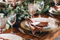 26 an elegant rustic fall tablescape with a greenery runner, tall candles in gold candlesticks, hammered chargers, pink glasses and dusty pink napkins