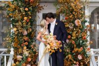 28 a refined and cool modern fall wedding arch composed of bold rust, yellow, mustard blooms and greenery and bright fall leaves