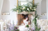 29 a refined wedding ceremony space with a chic fireplace, lots of white, peachy and purple overgrown blooms and a large mirror