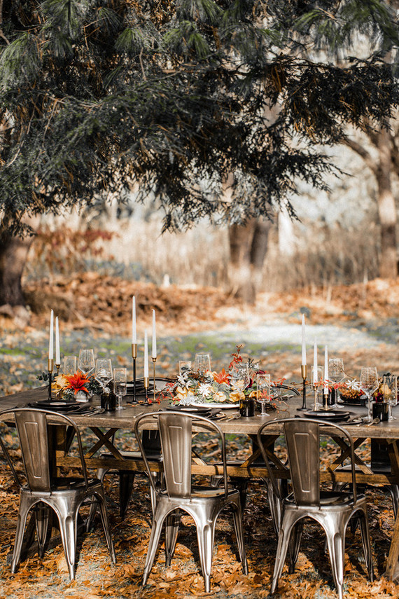 a modern moody fall wedding tablescape with tall candles, bright blooms and air plants, black plates and vases plus gilded and black candlesticks