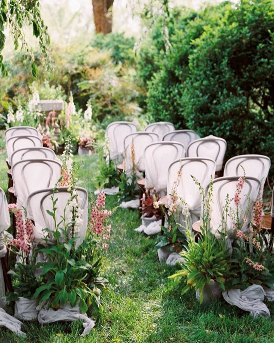 a beautiful and a bit wild wedding ceremony space on a lawn, with overgrown blooms lining up the aisle and an altar of the same blooms