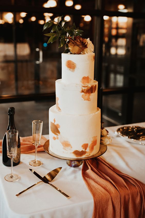 a chic modern fall wedding cake in white, with rust brushstrokes, a rust and a white rose and greenery on top is a very chic idea