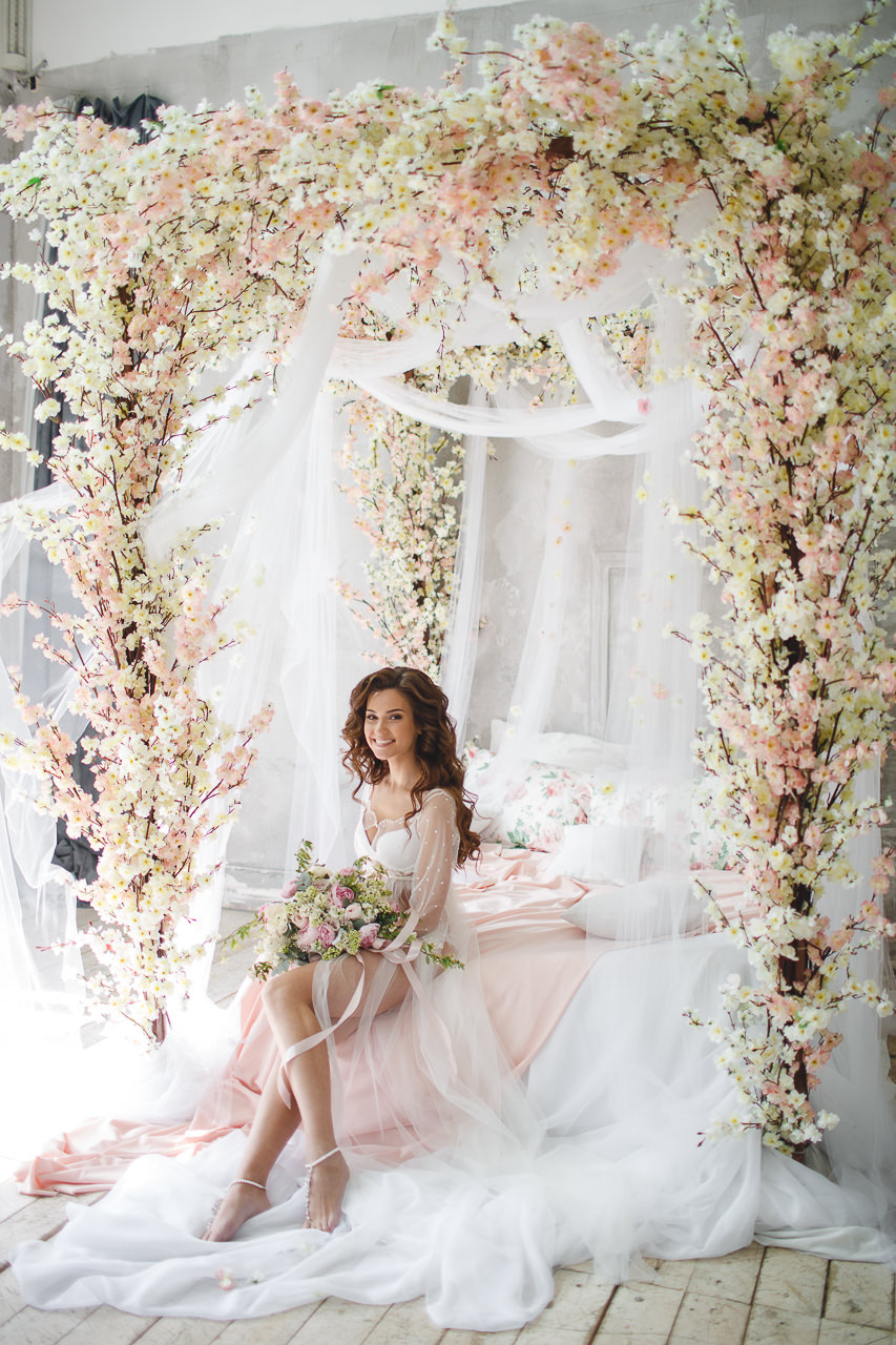 a canopy bed styled for bridal preparations with lots of pink and vanilla colored silk flowers is a creative and romantic idea