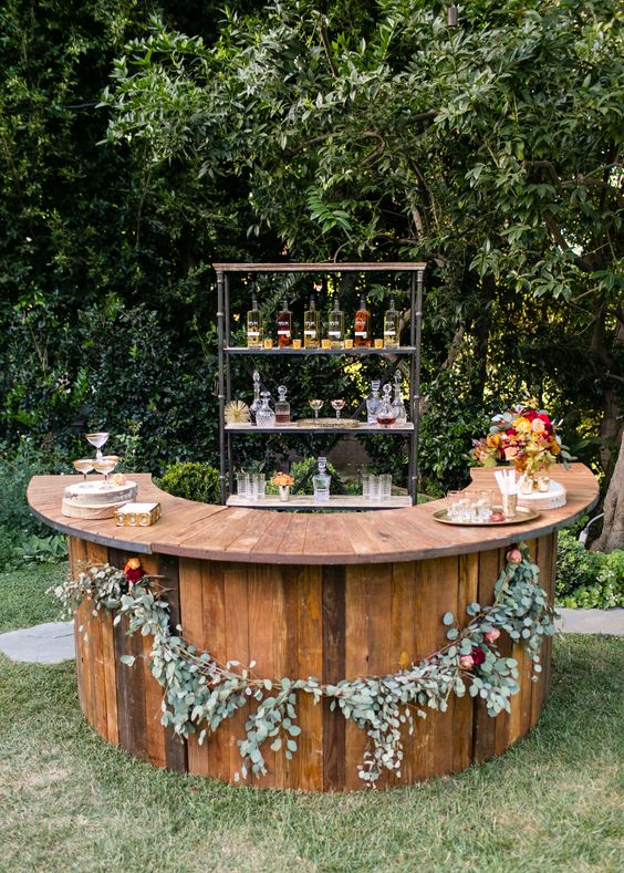 a stylish fall rustic wedding bar decorated with greenery and blooms plus a fall leaf arrangement on it is very cool