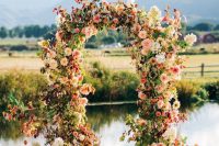 a beautiful and bright fall wedding arch of pink, blush and neutral blooms, greenery and bold foliage is a very cool and cheerful idea